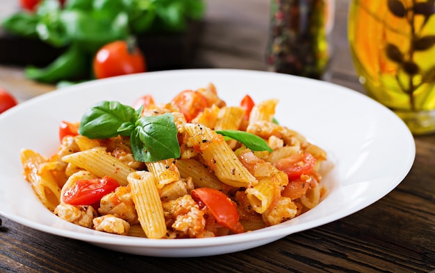 Penne-Teigwaren in der Tomatensauce mit Huhn, Tomaten, verziert mit Basilikum auf einem Holztisch. Italienisches Essen. Pasta Bolognese.