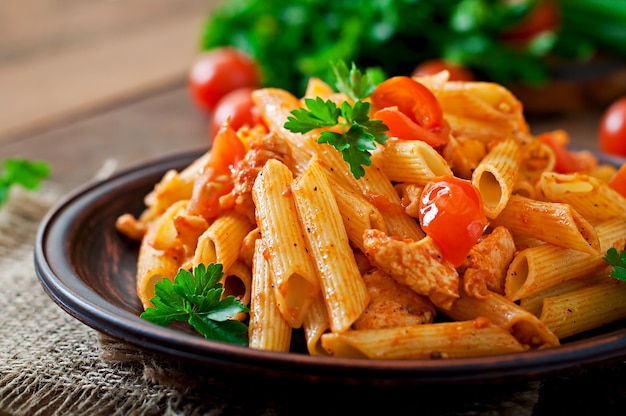 Penne-Teigwaren in der Tomatensauce mit Huhn und Tomaten auf einem Holztisch