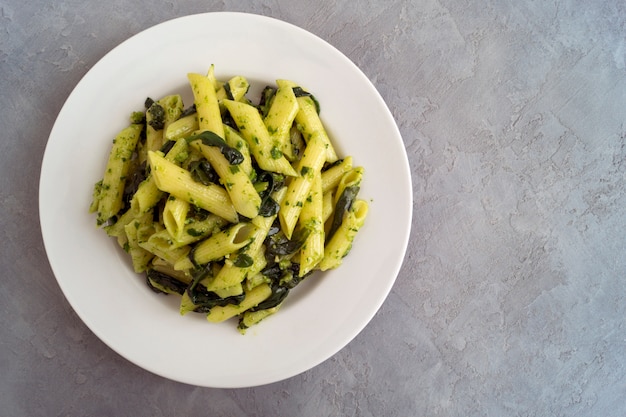 Penne-Teigwaren mit Spinat auf grauem Hintergrund.