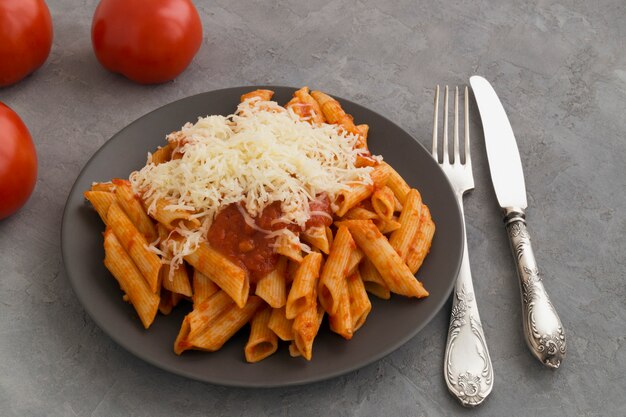 Penne-Teigwaren mit Tomatensauce auf grauem Hintergrund.