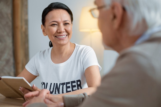 Pensamento sábio. Voluntário alegre e alegre sorrindo enquanto segura o caderno e olha para o homem mais velho