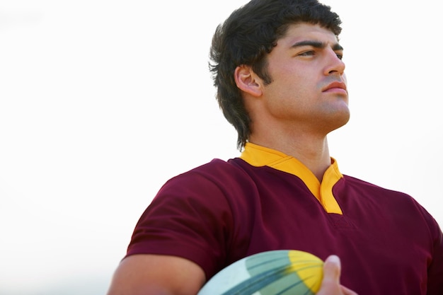 Pensamiento facial y jugador de rugby masculino con una pelota para estrategia de juego competitivo en un fondo blanco Idea de visión y atleta con un objeto para plan de acondicionamiento físico y uniforme de ejercicio deportivo