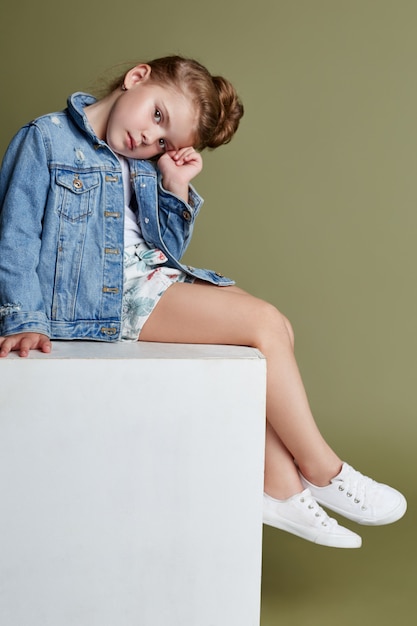 Pensamiento hermosa niña sentada en un cubo blanco y posando, modelos escolares