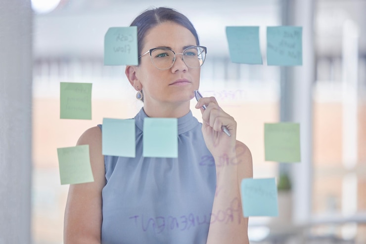 Foto pensamiento de planificación y mujer con estrategia de flujo de trabajo y scrum o ágil para objetivos de gestión de proyectos solución de ideas y resolución de problemas persona o trabajador de negocios con notas adhesivas en una placa de vidrio