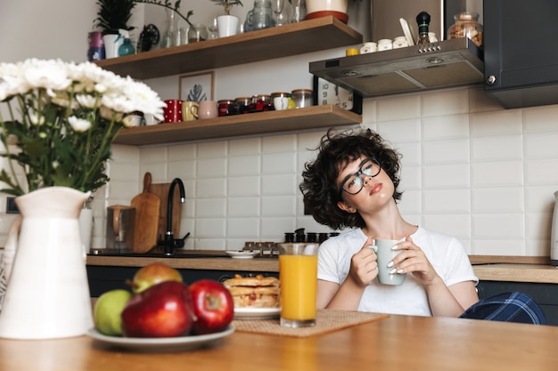 Pensamiento reflexivo mujer bastante rizada sentada en la cocina bebiendo té