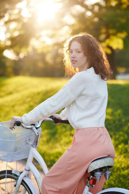 En pensamientos. Linda chica joven en bicicleta en el parque mirando pensativo