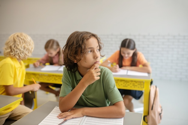 En pensamientos. Un niño sentado en el escritorio en el aula y pensando.