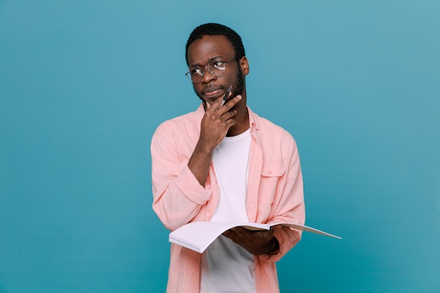 pensando agarrou o queixo segurando o notebook jovem afro-americano isolado em fundo azul