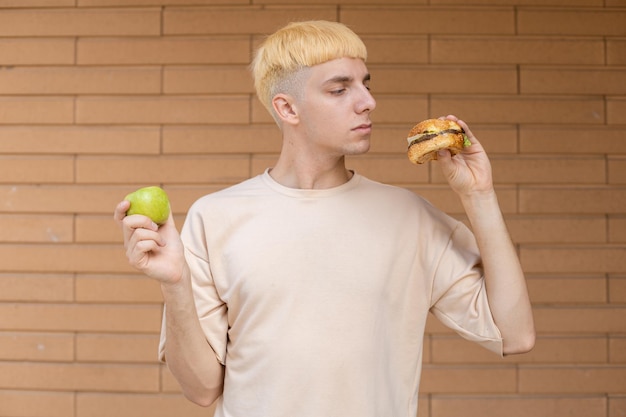 Pensando cara caucasiano segurando uma maçã verde em uma mão e um hambúrguer na outra