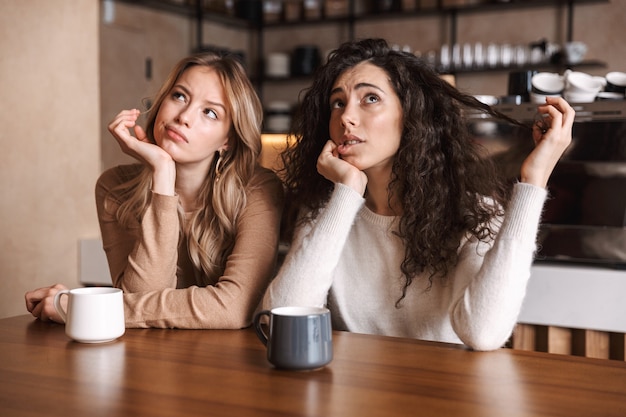 Pensando en jóvenes hermosas amigas sentadas en la cafetería mirando a un lado