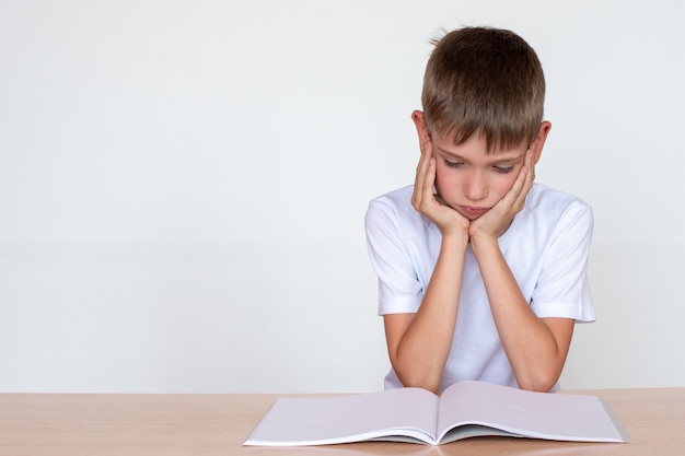 Pensando niño niño mirando en un cuaderno o libro, sentado en la mesa y haciendo la tarea