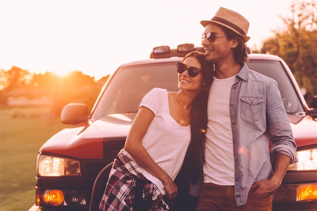 Pensando en un nuevo lugar al que ir. Hermosa joven pareja sonriente mirando pensativo mientras se vinculan entre sí y apoyándose en su camioneta pick-up