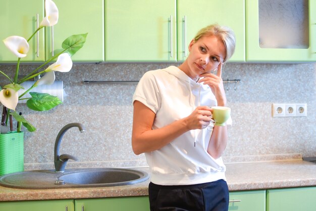 pensativa jovem loira com uma caneca de bebida na cozinha. contemplando um plano