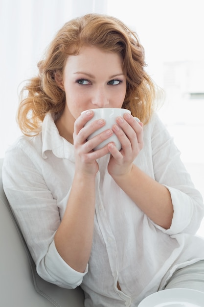 Pensativa joven bebiendo café en casa