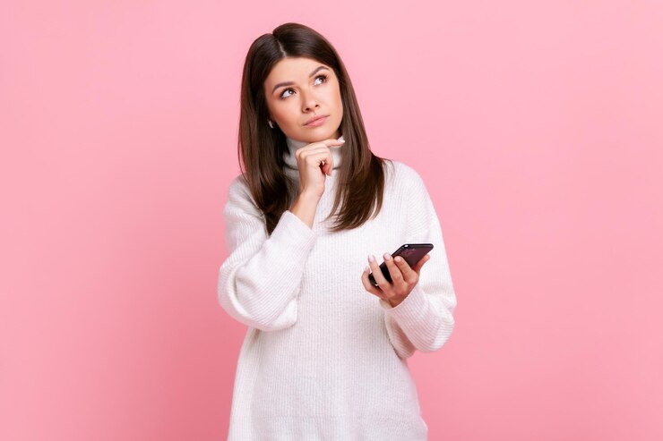 Foto pensativa linda jovem morena adulta segurando o telefone inteligente nas mãos olhando para longe pensando