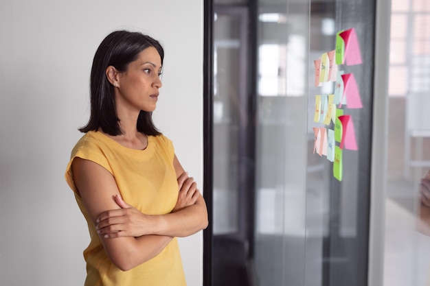 Foto pensativa mujer de negocios caucásica en la oficina de intercambio de ideas, leyendo notas en la pared de vidrio. trabajar en negocios en una oficina moderna.