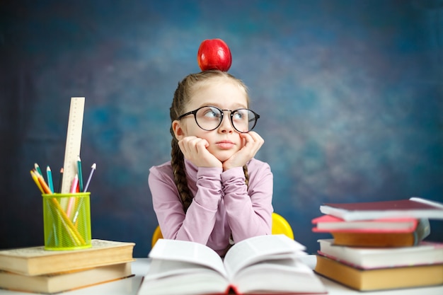 Pensativa niña de la escuela primaria con manzana en la cabeza teniendo una idea