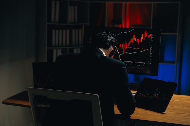 Pensativo, enfocado, exitoso, hombre caucásico, inversor bursátil, corredor, asesor financiero, se sienta en su escritorio de trabajo, mira la computadora, analiza pensativamente los riesgos y las perspectivas, sube o baja la moneda de criptomoneda.