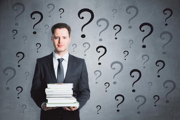 Pensativo hombre de negocios con libros y signos de interrogación Concepto de confusión e investigación