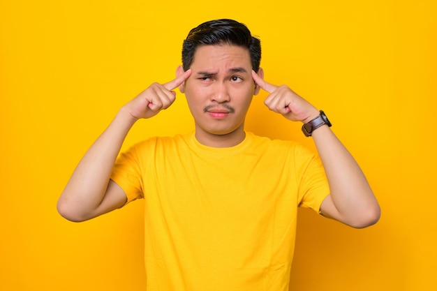 Pensativo jovem asiático em camiseta casual olhando para longe tentando se lembrar de algo isolado em fundo amarelo Conceito de estilo de vida de pessoas