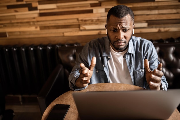 Pensativo jovem empresário afro-americano olhando para a tela do laptop discutindo o plano de negócios