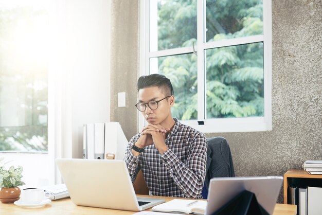 Pensativo joven empresario analizando datos en el informe en la pantalla del portátil