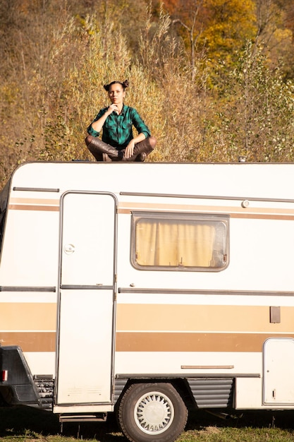 Pensativo, la niña se sienta en el techo de una caravana retro. Aventura de montaña