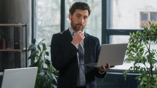 Pensativo perplexo homem de negócios caucasiano homem de negócios empreendedor masculino empregado corporativo gerente de vendas trabalhando no escritório digitando no laptop procurando informações na Internet escrevendo anotações analisando dados
