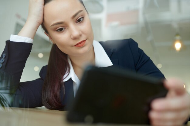 Pensativo serio bastante joven empresaria viendo seminario web en la pantalla de la computadora de la tableta