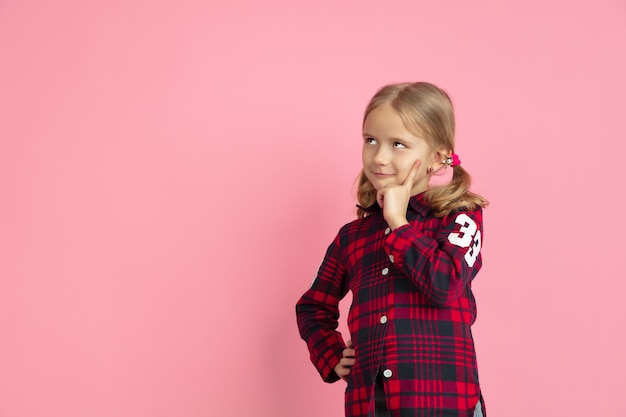 Pensativo, sonhando. Retrato da menina caucasiana na parede rosa.