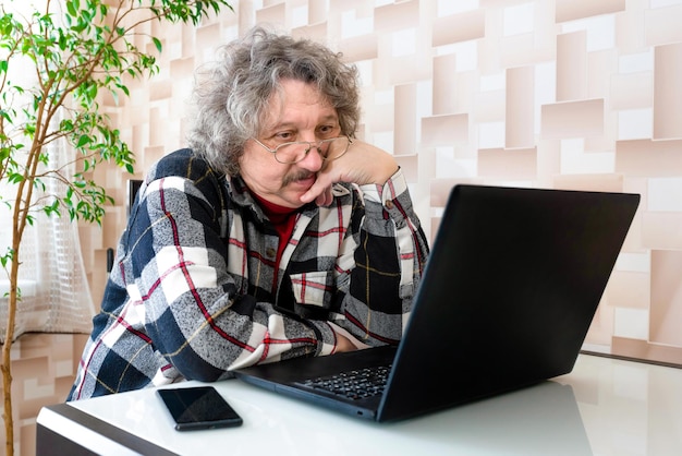 Pensionista adulto sentado à mesa na cozinha e lendo notícias no computador em casa
