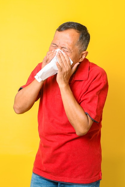 Pensionista asiático que se enferma con gripe y estornuda aislado de fondo amarillo