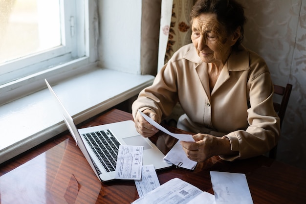 Pensionista lee innumerables trabajos y está muy concentrado. Mujer mayor cálculo de impuestos en casa. Mujer jubilada calculando sus facturas domésticas. Concepto de negocio, ahorros, seguro de anualidad, edad y personas