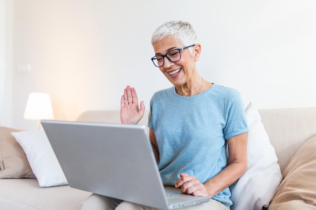 Pensionista progressista inteligente, entusiasta, anciã progressista agitando a mão e sentindo-se feliz enquanto usa uma videochamada em seu laptop e fala com os netos