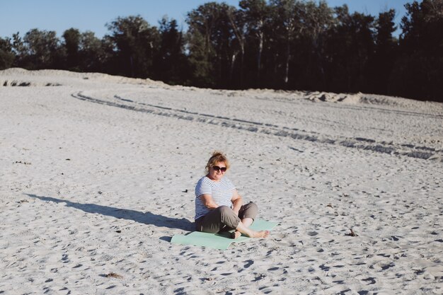 Pensionista sênior da mulher sentada na natureza na areia