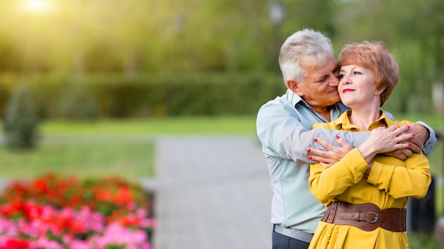Foto pensionistas de homem e mulher se abraçam gentilmente em um parque da cidade