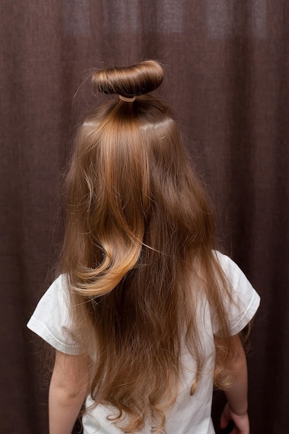 Penteado de menina trançado em uma trança fixada com um elástico azul closeup O penteado é feito com grampos e um elástico Apenas a parte de trás da cabeça com um corte de cabelo