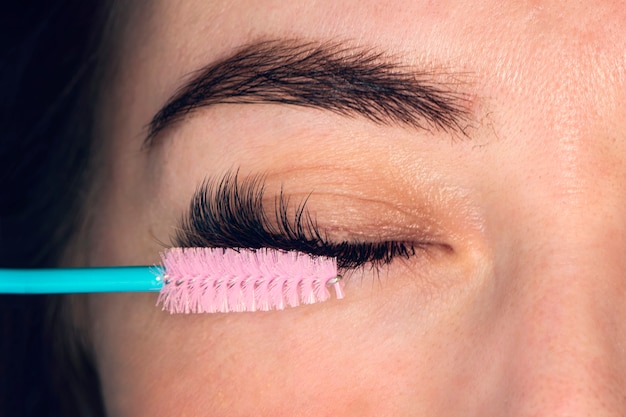 Foto penteando os cílios estendidos. olho de mulher com bela maquiagem e cílios longos. pincel de rímel. tratamento para cílios: levantamento de pestanas, coloração, ondulação, laminação e extensão para pestanas.