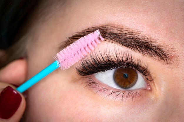 Penteando os cílios estendidos Uma garota de olhos castanhos faz uma maquiagem de close-up Jovem mulher bonita aplicando maquiagem de rímel nos olhos por pincel