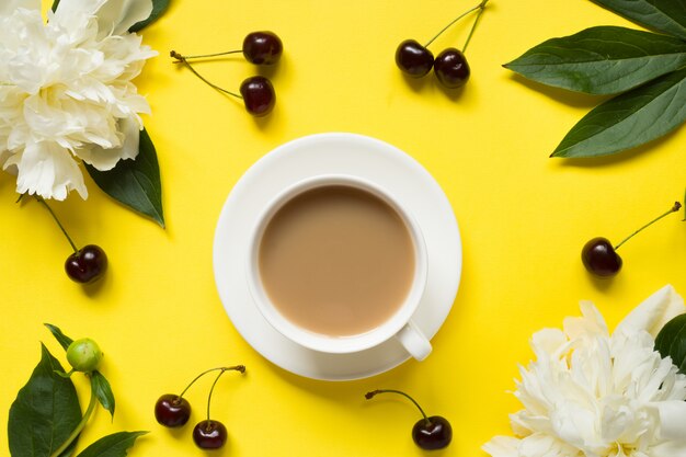 La peonía blanca florece la taza de las bayas de la cereza de café en fondo brillante amarillo.