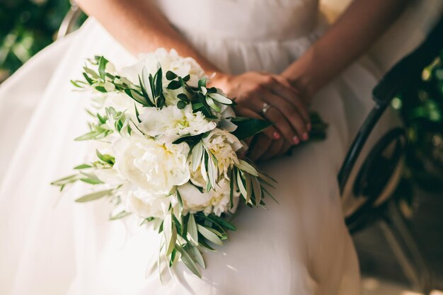 Peônias brancas de buquê de casamento e mãos de noiva fecham