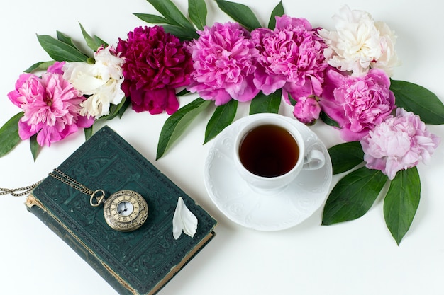 Peonías, cogollos, una taza de té, un viejo reloj de bolsillo y un libro.