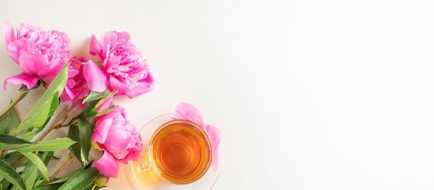 Foto peonías rosas frescas brillantes y una taza de té en una taza y plato transparente sobre un fondo claro. copyspace, vista superior. lindo y acogedor plano femenino elegante.