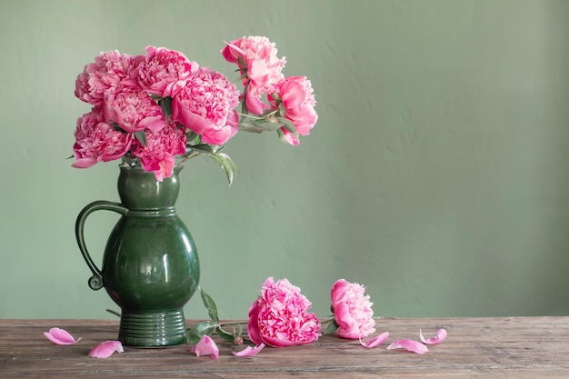 Peonías rosas en jarra de cerámica sobre fondo verde