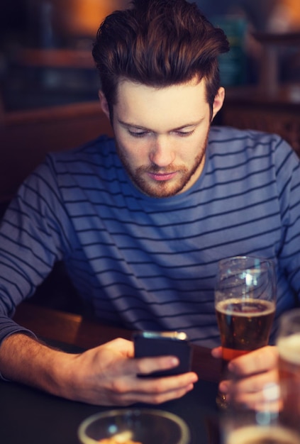 People and Technology Concept - Mann mit Smartphone trinkt Bier und liest Nachricht an der Bar