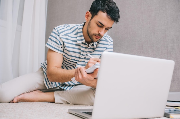 People Business- und Lifestyle-Konzept Fokussierter junger kaukasischer Mann, der auf dem Boden im Raum vor einem offenen Laptop-Computer sitzt Ernsthafte europäische männliche Schüler lernen Lektion