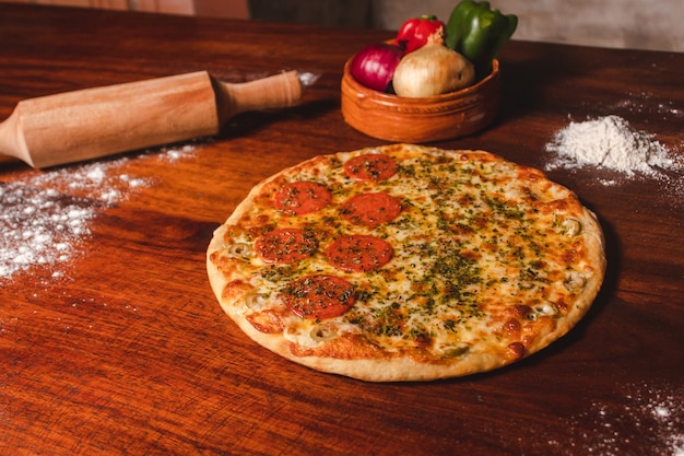 Peperoni-Pizza mit viel Käse und vielen Belägen auf einem Holztisch.