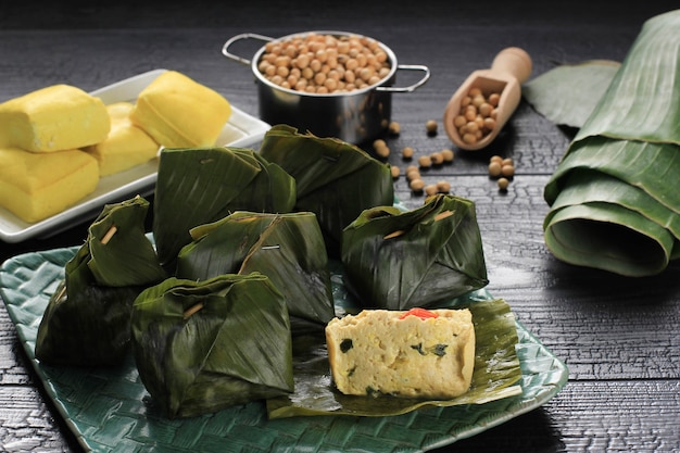 Pepes Tahu ist indonesischer Gewürztofu, der mit Bananenblättern umwickelt und gedämpft wird, typisch indonesisches Essen aus West-Java (Sundanesisch). Gedämpfter Tofu mit asiatischem Basilikum. Serviert auf gewebtem Teller, schwarzer Hintergrund