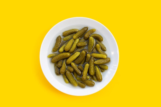 Pepinillos o pepinos en escabeche en un tazón blanco sobre fondo amarillo.