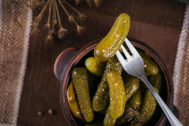 Pepinillos, pepino encurtido en un tenedor, plato de verduras marinadas en la superficie de madera rústica. Comida limpia, concepto de comida vegetariana